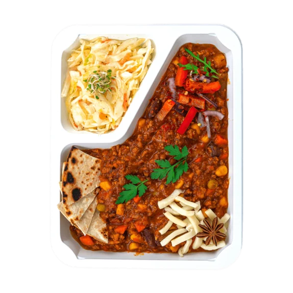 Danie podzielone na trzy części: chili con carne z warzywami i czerwonymi paprykami, ozdobione natką pietruszki, obok starty ser i anyż gwiazdkowy. W mniejszej przegródce znajduje się surówka z białej kapusty z kiełkami, a poniżej kawałki podpieczonej tortilli.