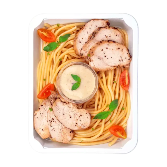 Danie w białym pojemniku: spaghetti z grillowanym kurczakiem w plasterkach, pomidorkami koktajlowymi i listkami bazylii. Pośrodku znajduje się mały pojemniczek z jasnym sosem, ozdobiony listkiem bazylii.